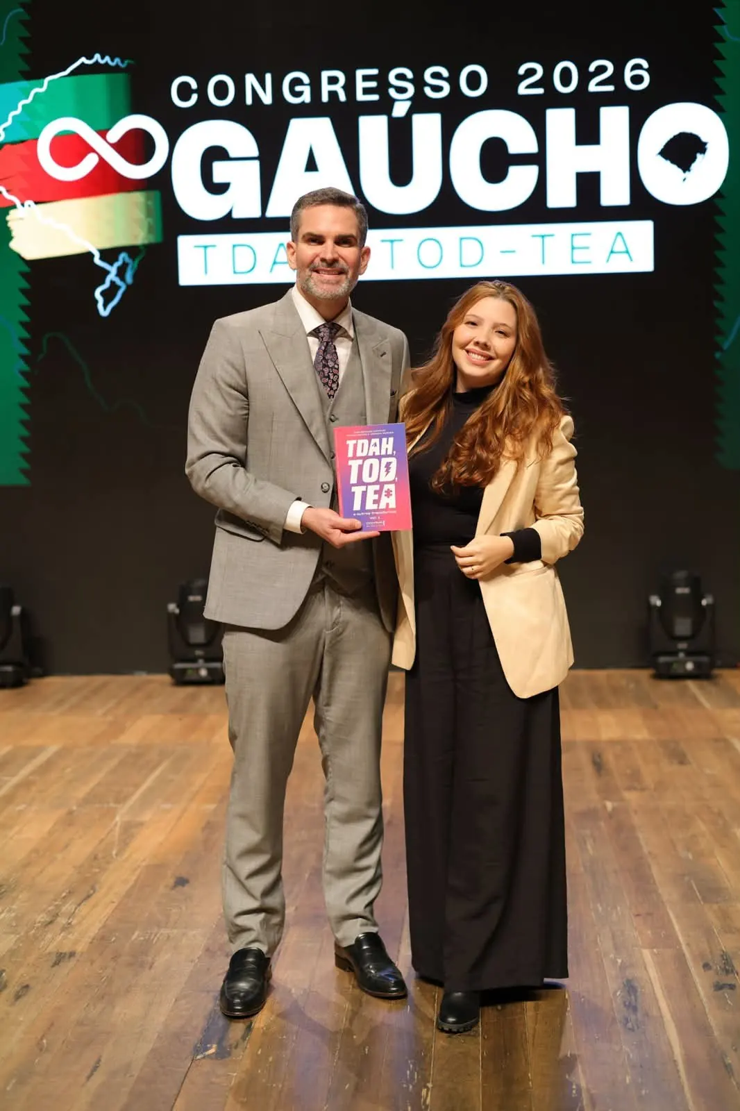 Brunna no palco do Congresso Gaúcho 2026 de TDAH, TOD e TEA, com o livro TDAH, TOD, TEA